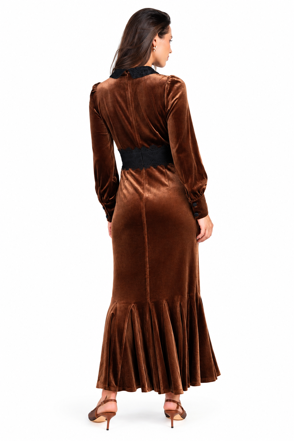 A woman viewed from the back wearing a long brown velvet dress with a black collar, black waistband, and black ruffled hem, paired with brown heeled sandals, against a plain white background.