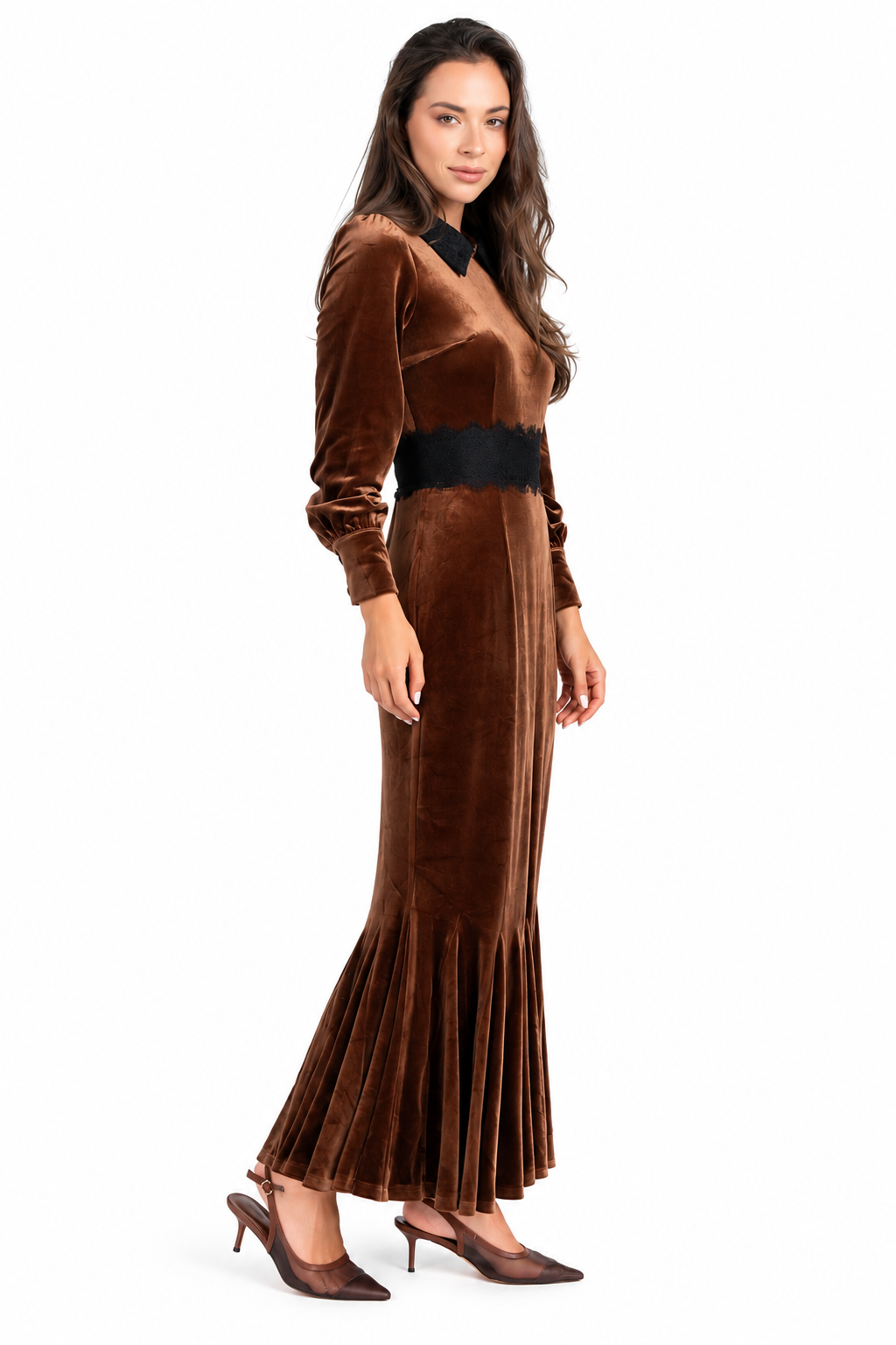 A woman modeling a long-sleeved brown velvet maxi dress with a black collar and a wide black waistband, paired with brown pointed-toe heels, against a plain white background.