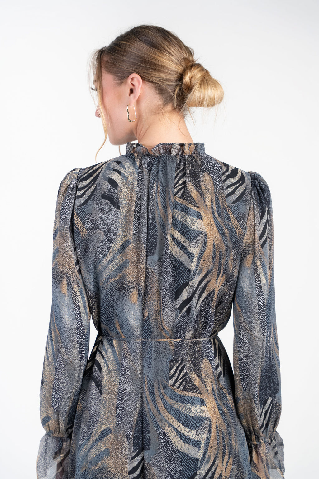 A woman shown from the back wearing a long-sleeve dress with a textured abstract pattern in slate blue, gray, and warm tan tones, set against a plain white studio background.