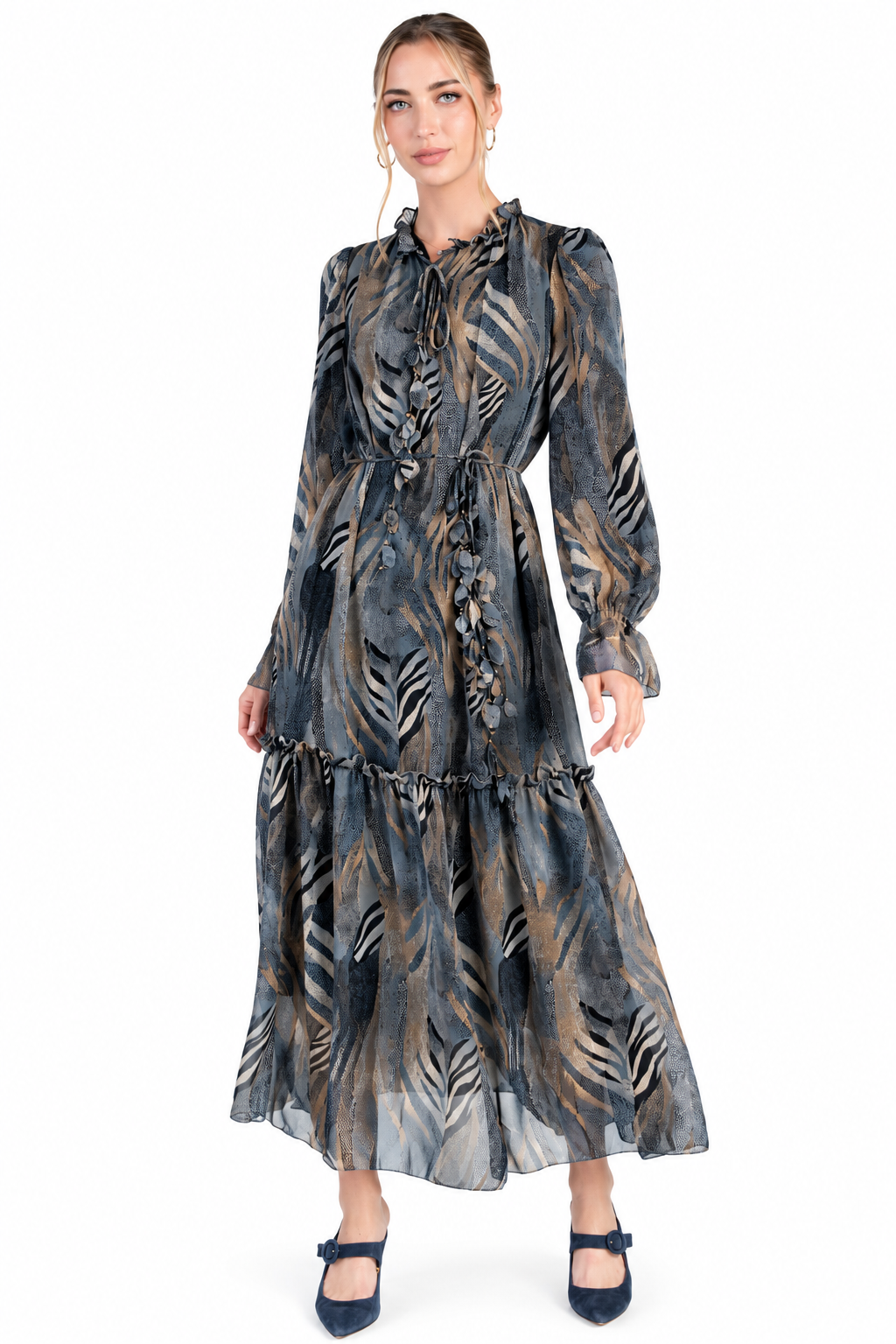A woman modeling a long-sleeved midi dress with a tiered skirt and an abstract botanical print in gray, black, and brown tones, paired with dark blue shoes against a plain white background.