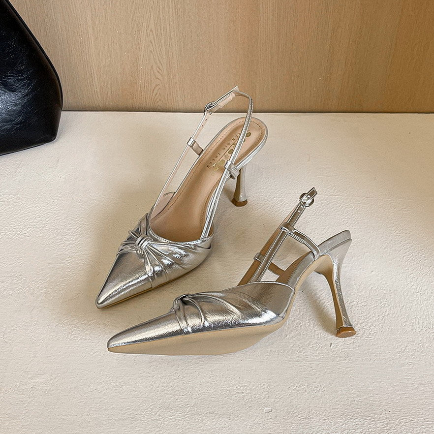 A pair of metallic silver pointed-toe slingback high heels with a knotted detail on the toe, displayed on a light white surface.