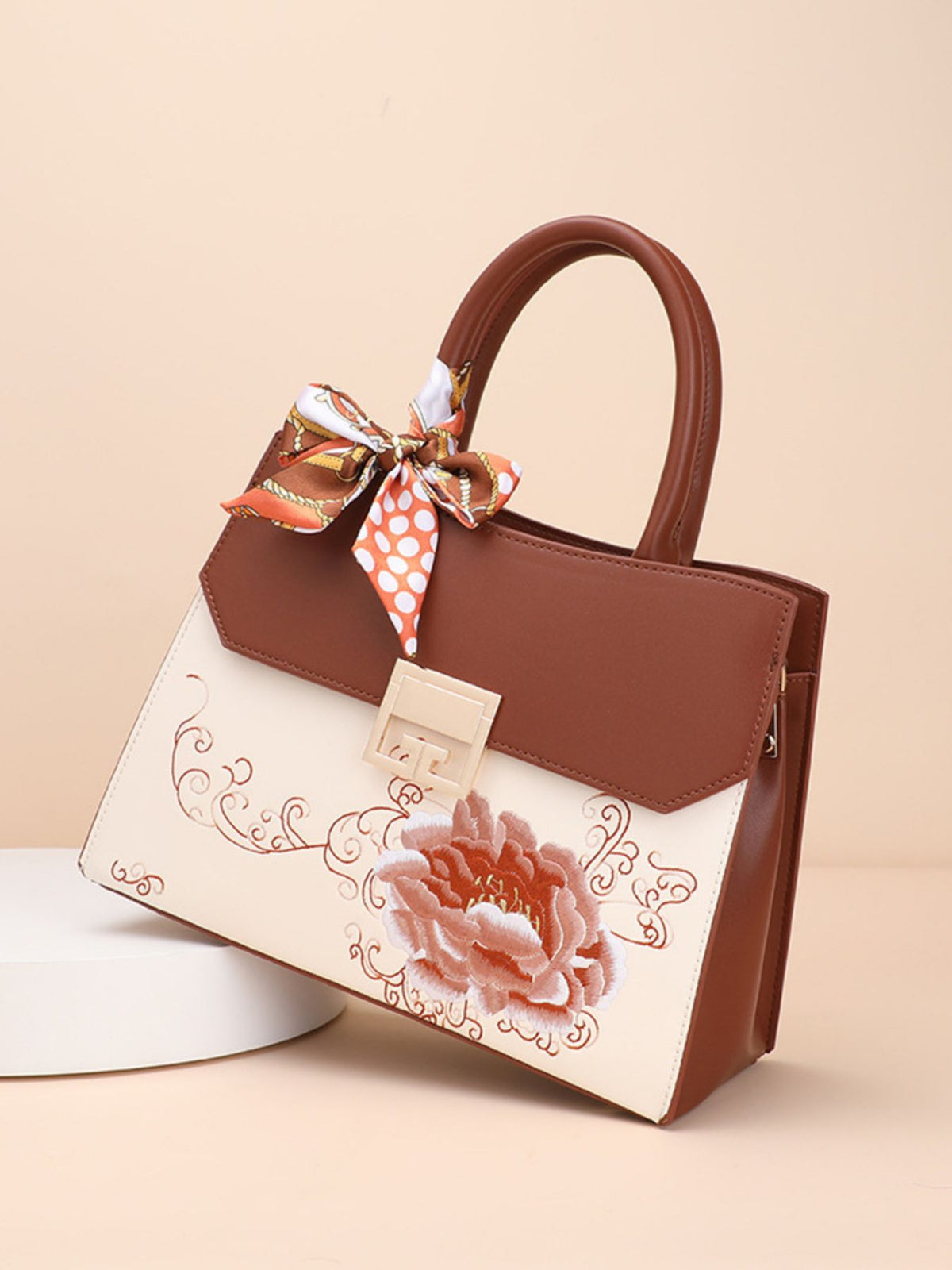 Brown handbag with floral design and bow on a beige background