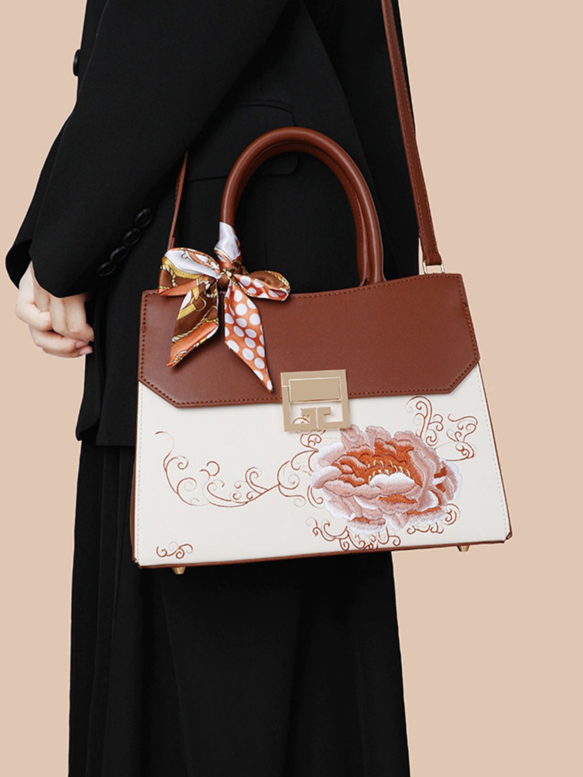 Brown handbag with floral design and bow held by a person against a beige background