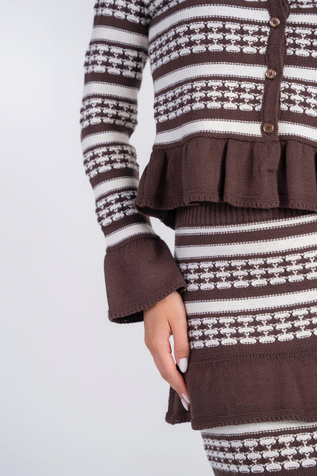 A close-up of a brown and cream knit outfit featuring a long-sleeve top with a ruffled peplum hem and matching skirt, worn by a model.