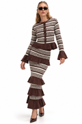 A woman modeling a matching two-piece knit set with a brown and cream houndstooth pattern, featuring a long-sleeve top with ruffled cuffs and a tiered skirt, against a plain white background.