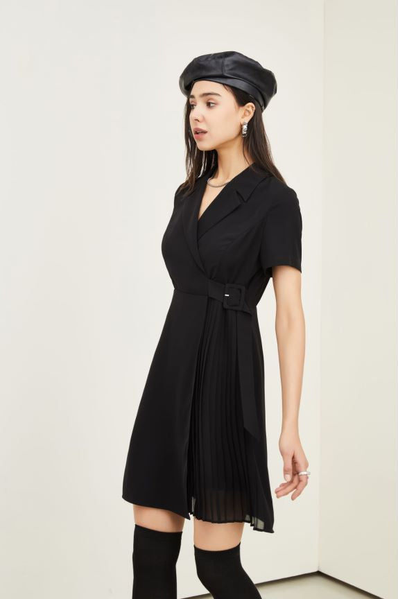 A woman modeling a black short-sleeve wrap-style pleated dress with a matching black beret and black knee-high socks against a plain off-white studio background.