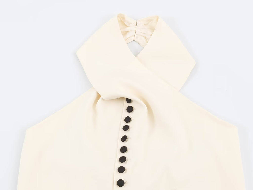 A cream-colored halter top with a unique criss-cross collar design and a vertical row of black buttons down the center, shown against a plain white background.