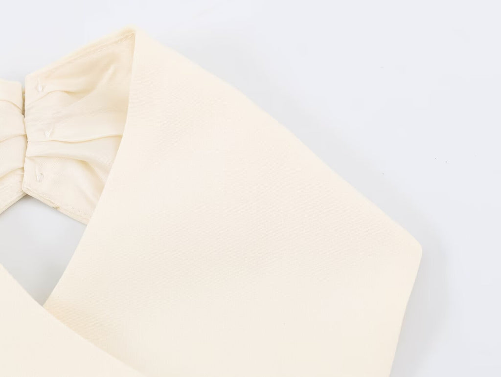 A close-up of a cream-colored fabric garment, showing a wide strap or band and a gathered elasticized section, laid flat on a white background.