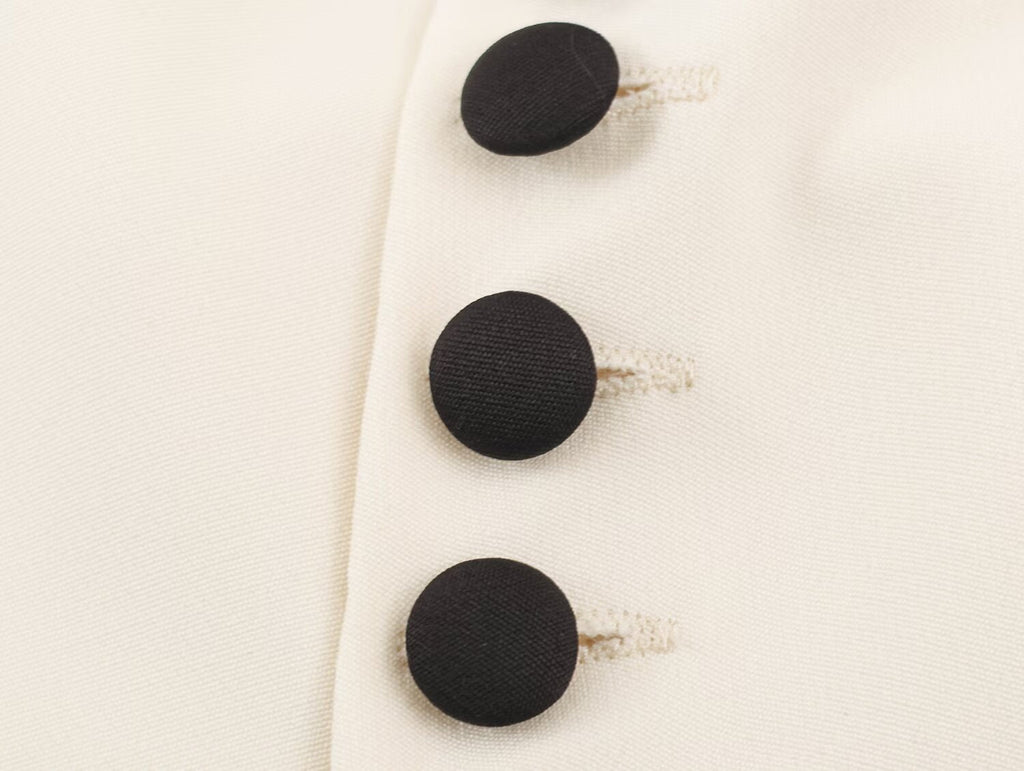 Close-up of a cream-colored fabric garment featuring three large, round black buttons with decorative white thread loops.
