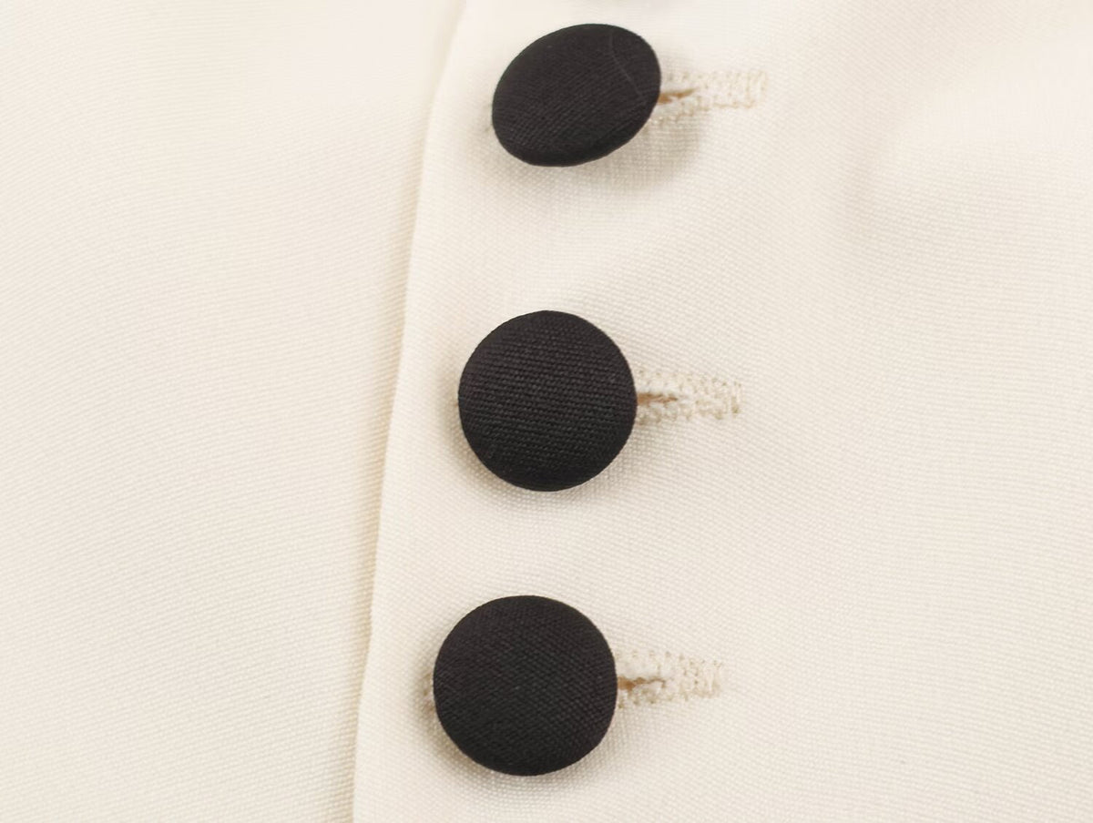 Close-up of a cream-colored fabric garment featuring three large, round black buttons with decorative white thread loops.