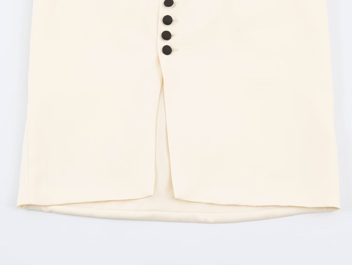 Close-up of a cream-colored garment with a front slit and a vertical row of black buttons, shown against a plain white background.