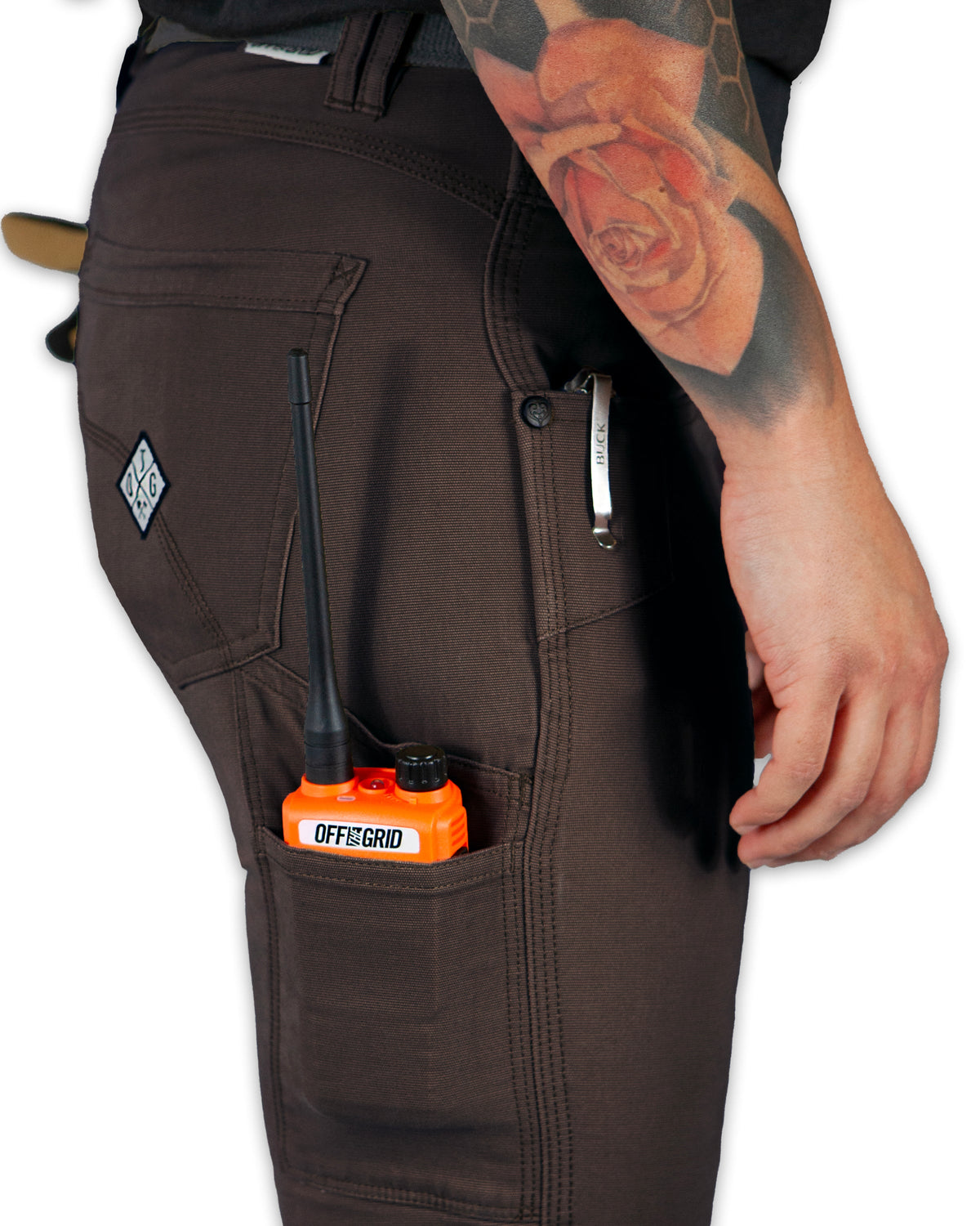 Person wearing brown pants with a tool in an orange case attached to the pocket, on a white background.