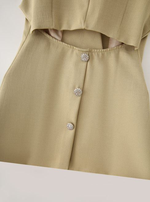 Close-up of a beige or light khaki textured fabric garment with a waist cutout and three decorative silver rhinestone buttons down the front.