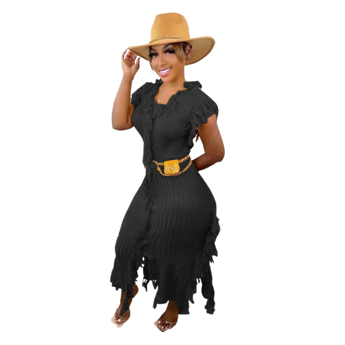 A woman modeling a black fringed maxi dress with a matching gold belt and a tan wide-brim hat, set against a plain white background.
